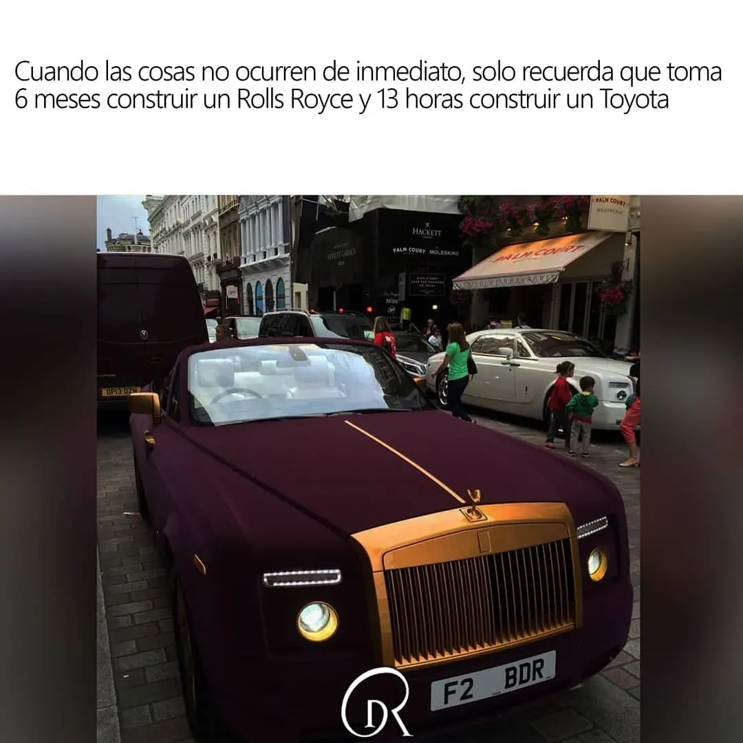Se ve un Rolls Royce de color granate y dorado aparcado en una calle de Londres. El coche está rodeado de gente que lo mira y le hace fotos. El coche es muy bonito y llama la atención por su color y su diseño.